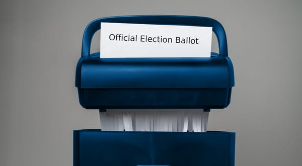 A piece of paper with the text "Official Election Ballot" inserted into a USPS-colored paper shredder